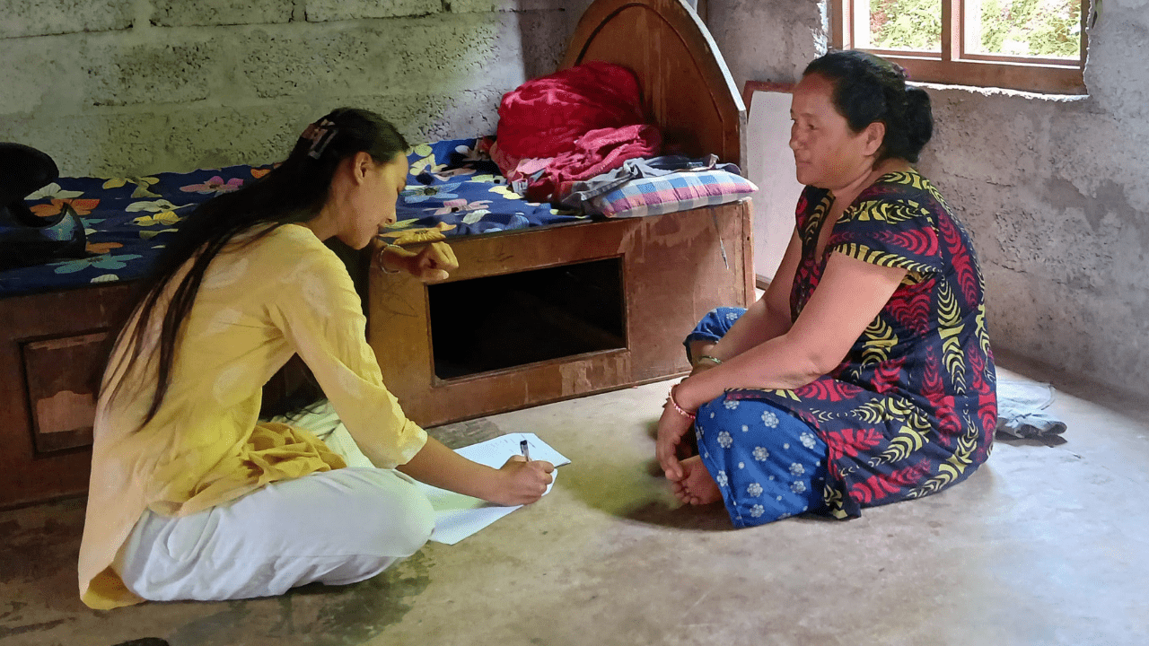 Two women sitting on the floor indoors talking one taking notes