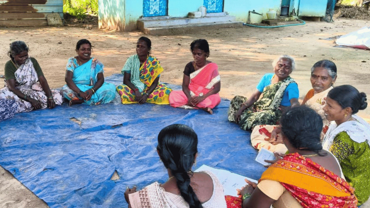 Group of people sitting in a circle on the floor outside