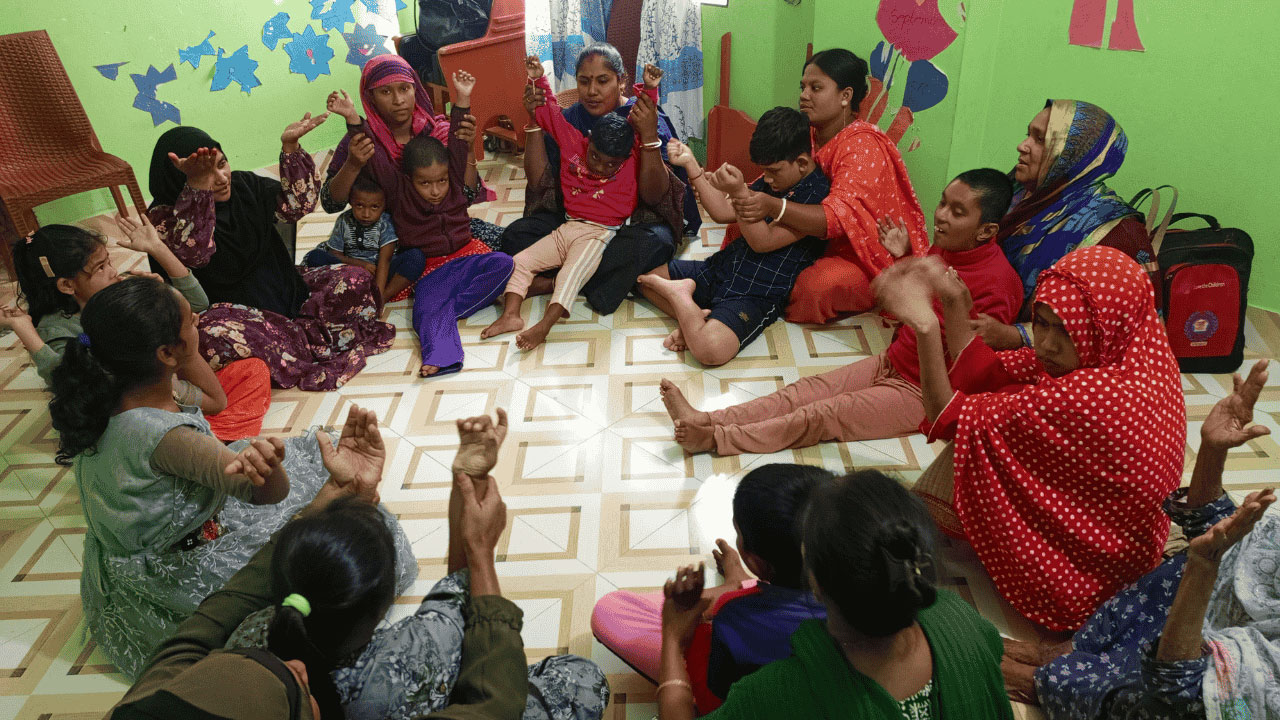 A group of women and children sitting indoors in a circle on the floor