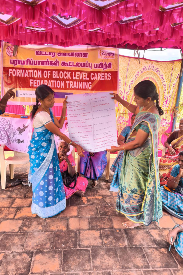 Two women standing and holding a large piece of paper between them which they are presenting to the group