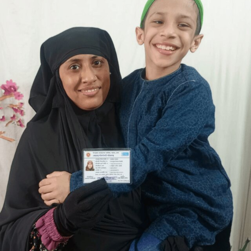 Image of a woman holding up an ID card in one hand with the other around her child