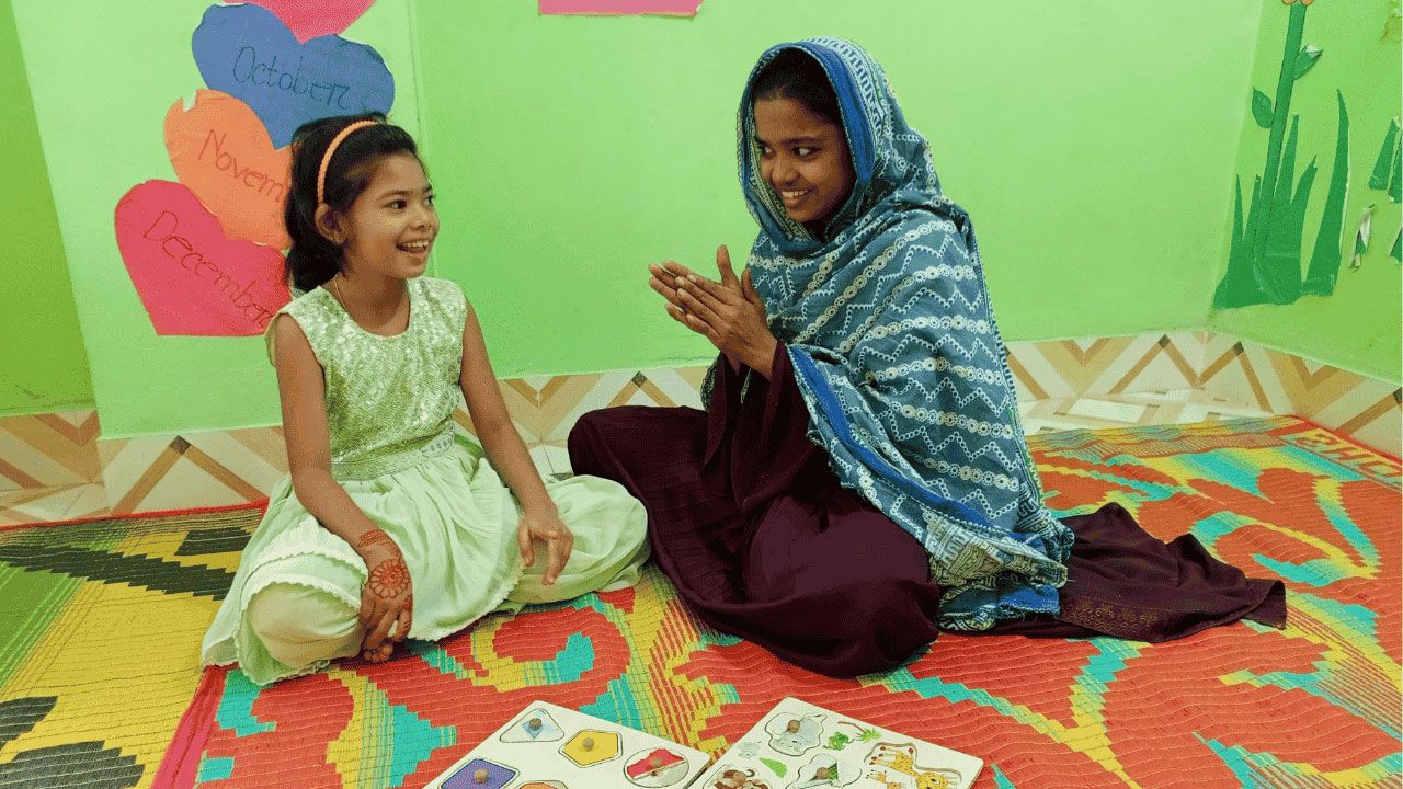 Two girls sitting on the floor, surrounded by open books, engaged in reading and sharing ideas.