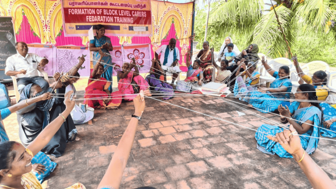 Group of people sitting on the floor in a circle each holding the end of a piece of string which are meeting in the middle