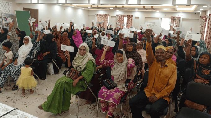 Large group of people sitting inside holding up ID cards