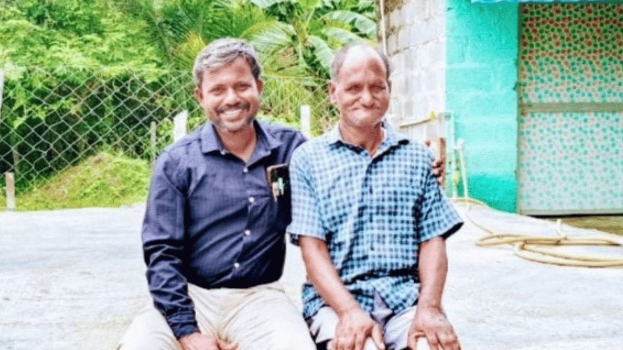 Two men sitting outside on a low wall smiling