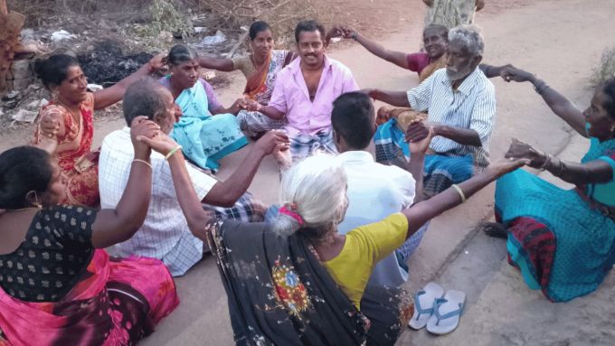 Group of people sitting in a circle onthe floor holding hands